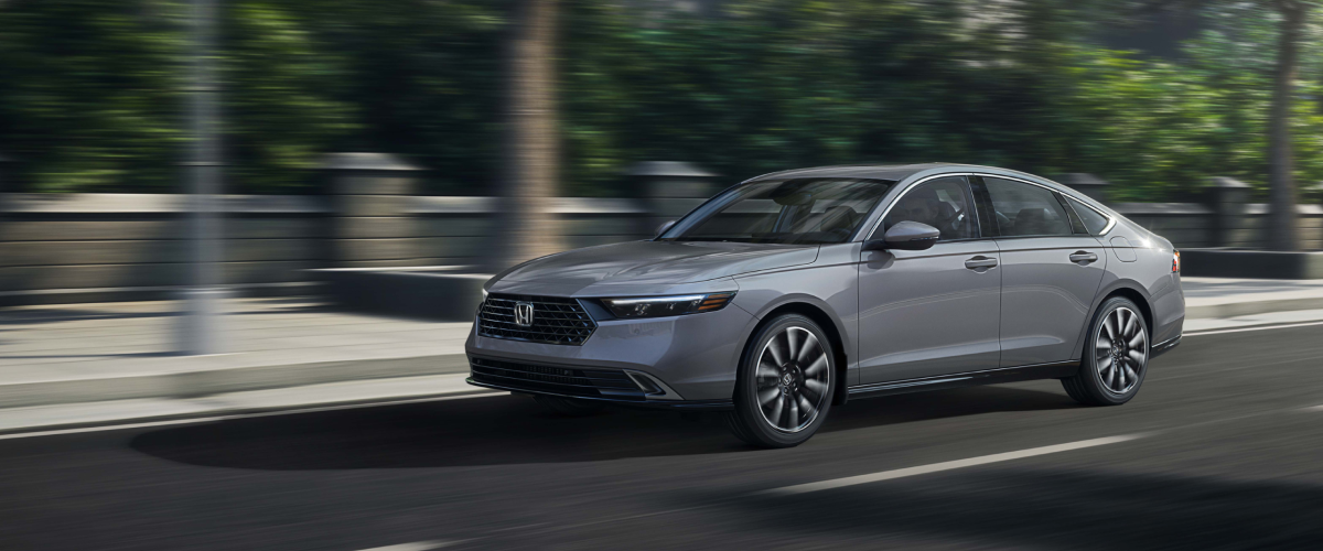 3/4 front view of grey Accord driving on upper-class city street lined with trees.
