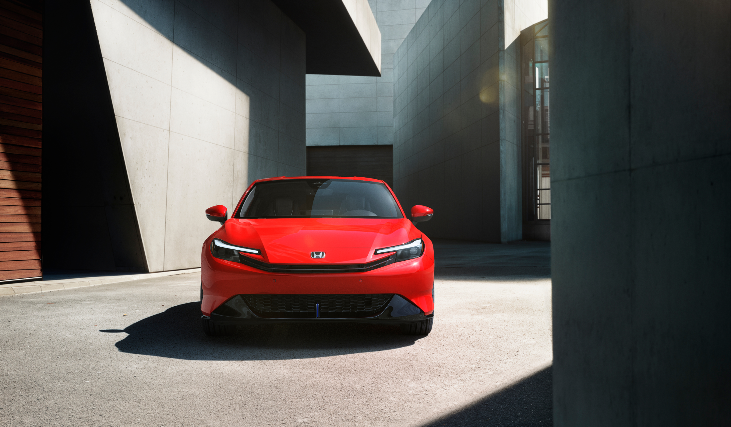 Front view of a red Prelude parked between stone-walled buildings in the sunshine.  
