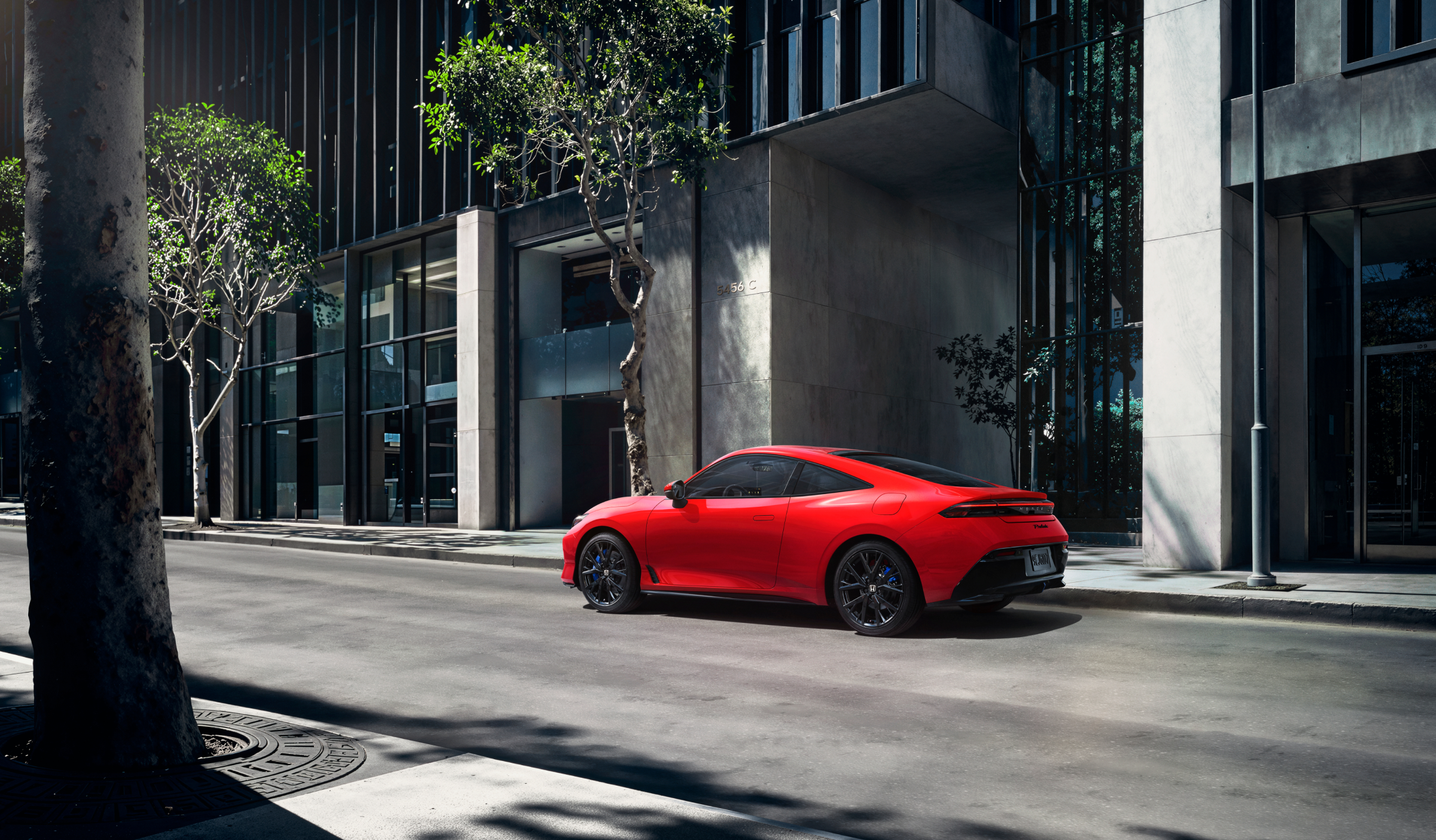 3/4 rear side view of a red Prelude driving on a tree-lined city street.