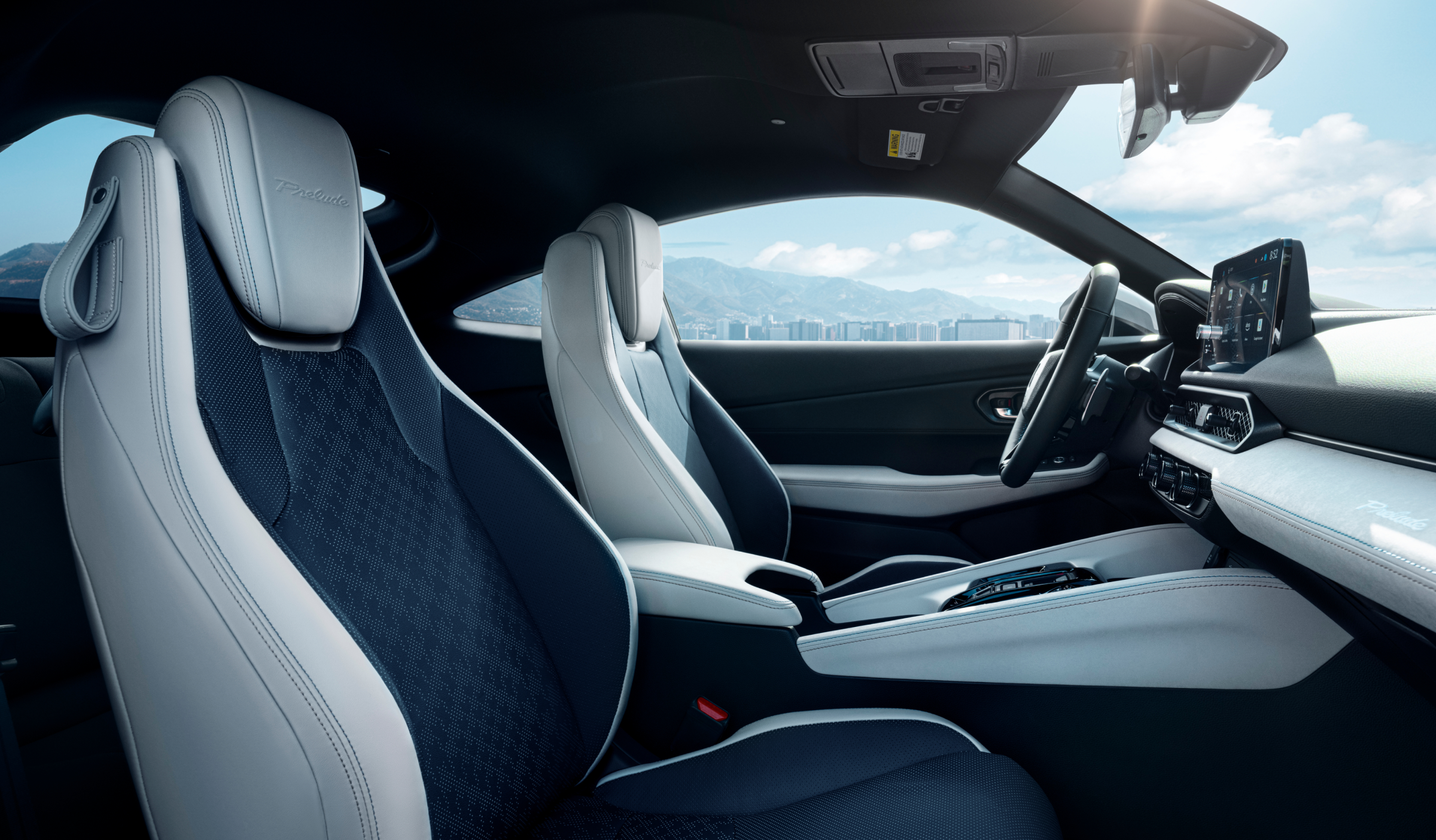 Passenger's side view of Prelude's black and white front row seats. Out the driver's side window are hills and trees.