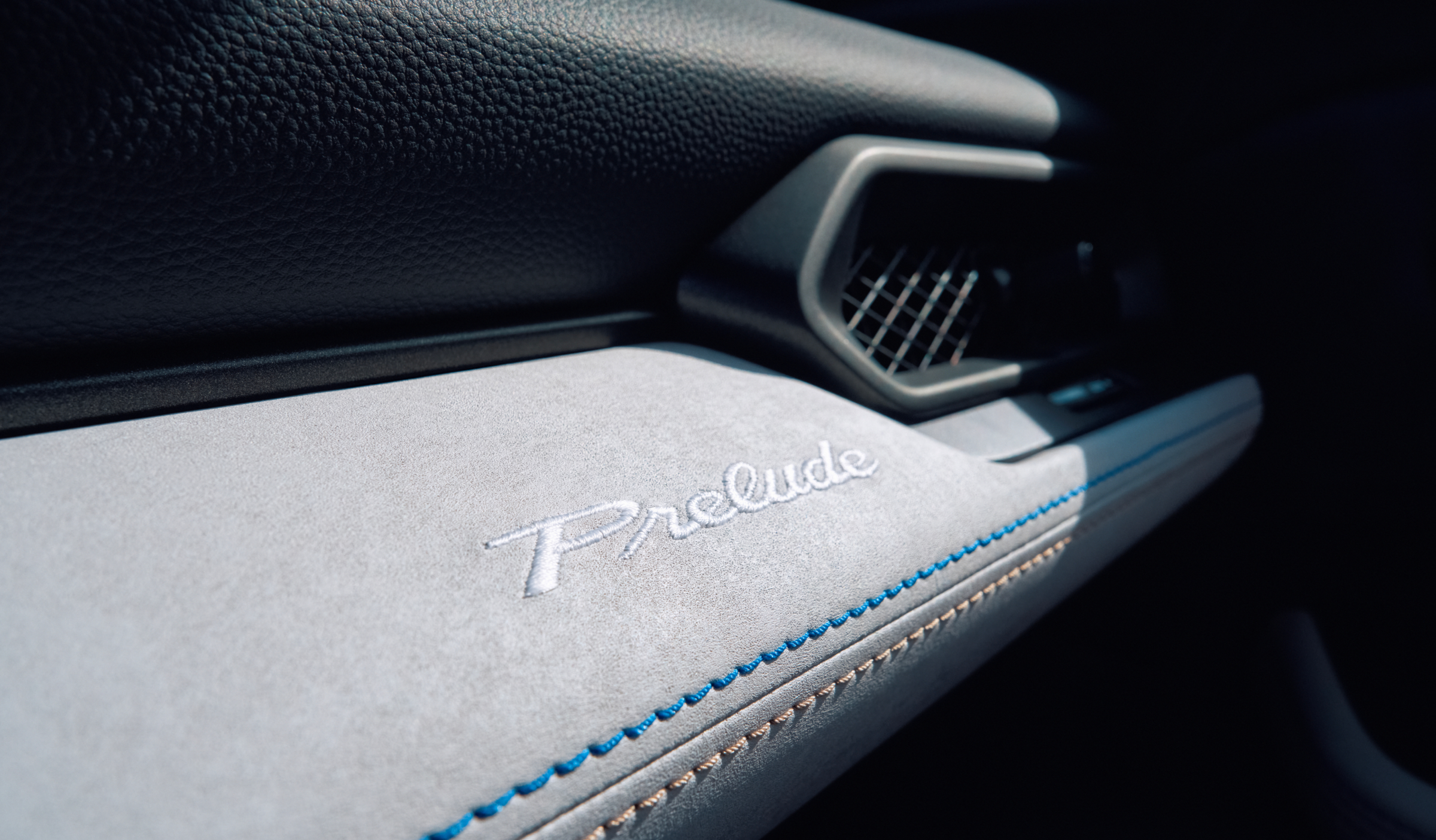 Closeup of Prelude's grey dashboard with blue and cream contrast stitching and stitched Prelude logo. 