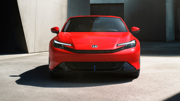 Front view of a red Prelude parked between stone-walled buildings in the sunshine.  